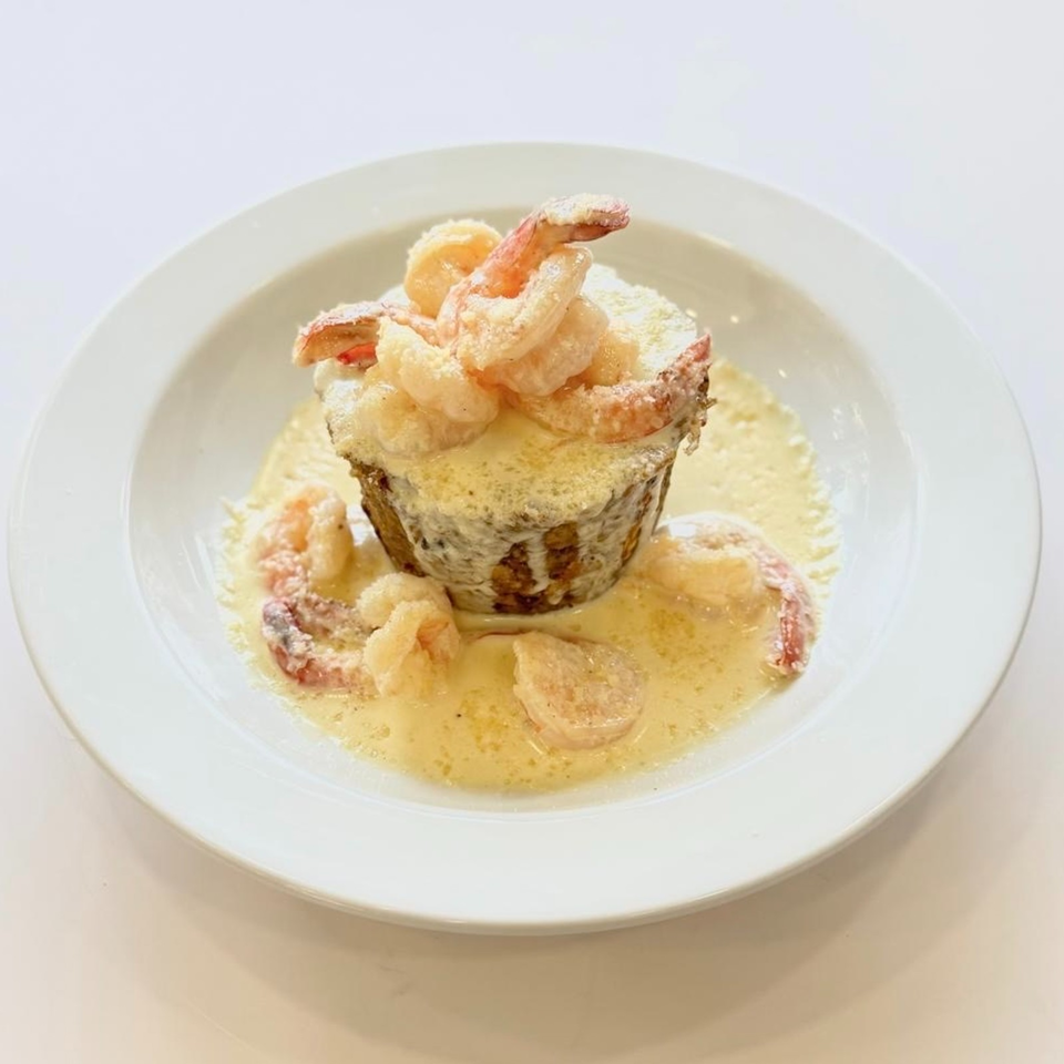 Golden fried shrimp arranged over a creamy, sauce-covered savory centerpiece on a white plate.